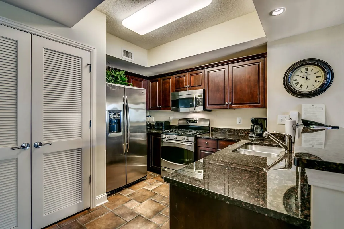 A warm and inviting kitchen featuring stainless steel appliances, granite countertops, and wooden cabinets. The spacious layout provides ample counter space for meal preparation, with modern conveniences clearly visible. Decorative touches like a clock on the wall add to the homey atmosphere.