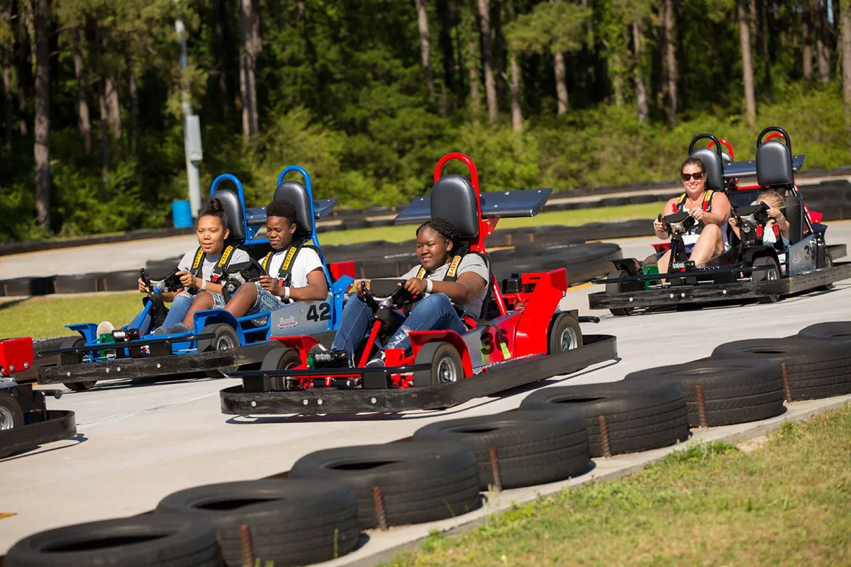 An energetic exterior scene at a go-kart track, with participants racing along the track, colorful tires lining the way, and spectators enjoying the activity. The shot captures a sense of fun and social interaction.